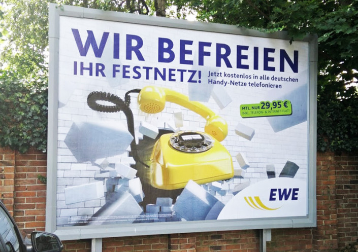 Frese & Wolff Werbeagentur, Großfläche für EWE, zu sehen ist ein gelbes Telefon, das eine Mauer durchbricht, dazu der Text "Wir befreien Ihr Festnetz, jetzt kostenlos in alle deutschen Handynetze telefonieren"